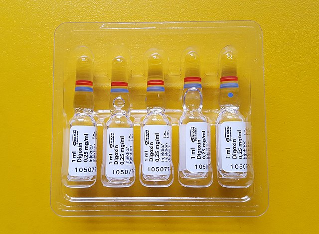 5 vials of digoxin medicine in a plastic container, placed on a bright yellow table.
