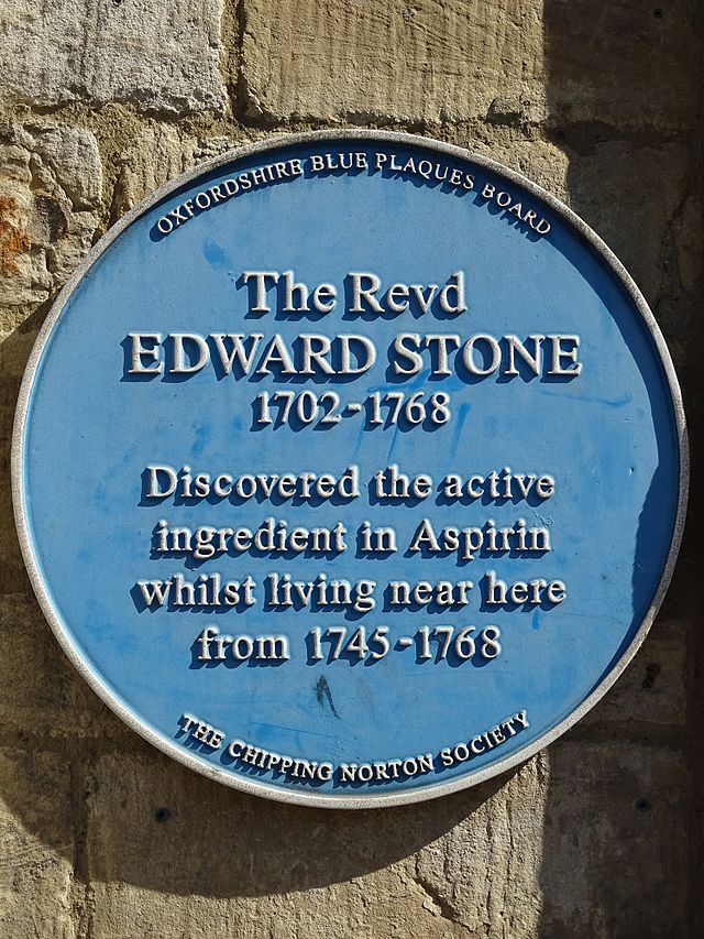 The blue round sign reads: "OXFORDSHIRE BLUE PLAQUES BOARD. The Revd, EDWARD STONE, 1702-1768. Discovered the active ingredient in Aspirin whilst living near here from 1745-1768. THE CHIPPING NORTON SOCIETY.".